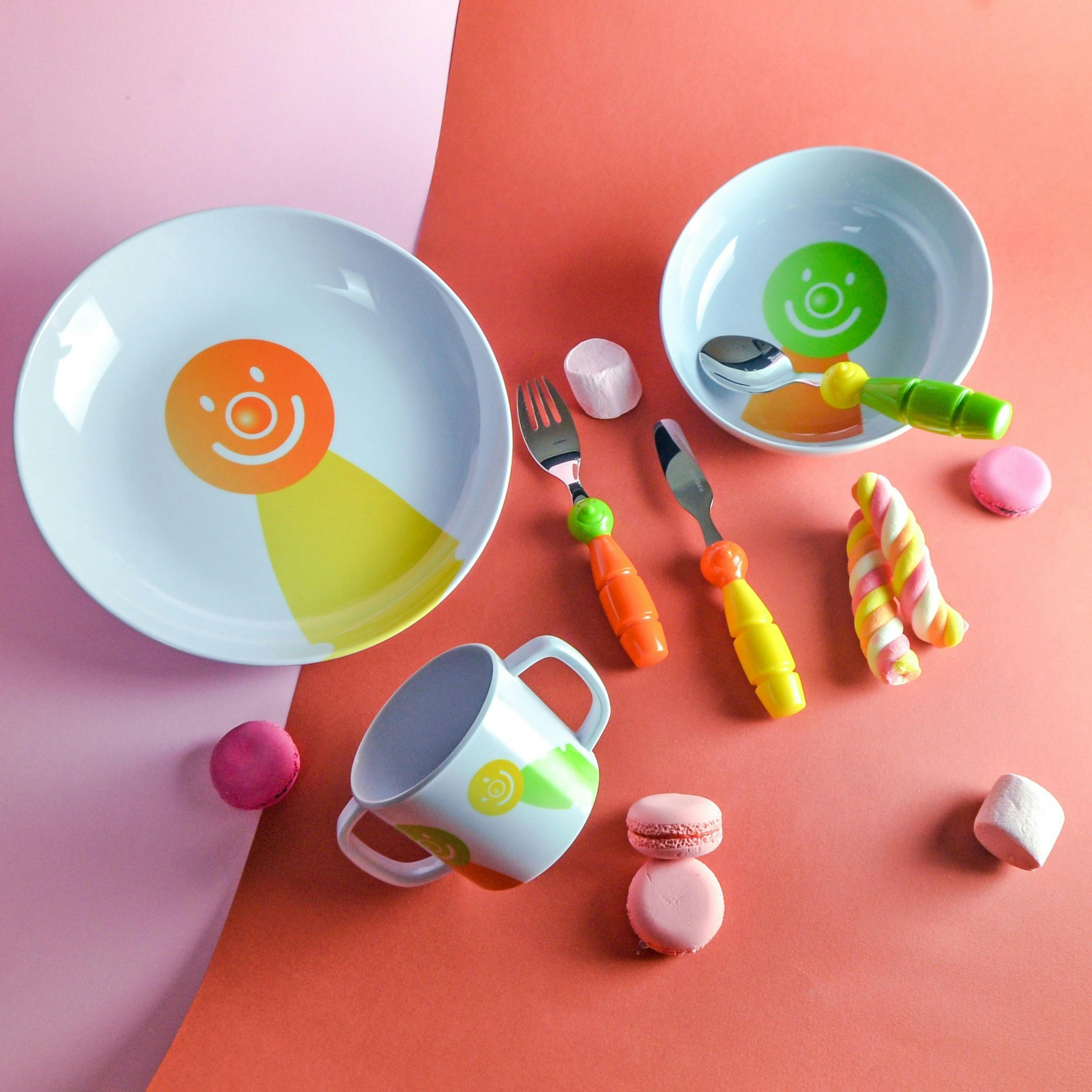 children's brightly colored plastic melamine plates, cup, and utensils on a bright pink and orange background