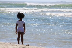 A little girl looks out from the beach into the ocean- climate and child care