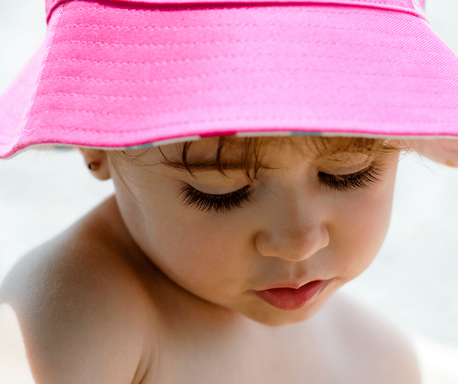 Young child wearing a pink bucket hat sitting in the sun--Seguridad solar