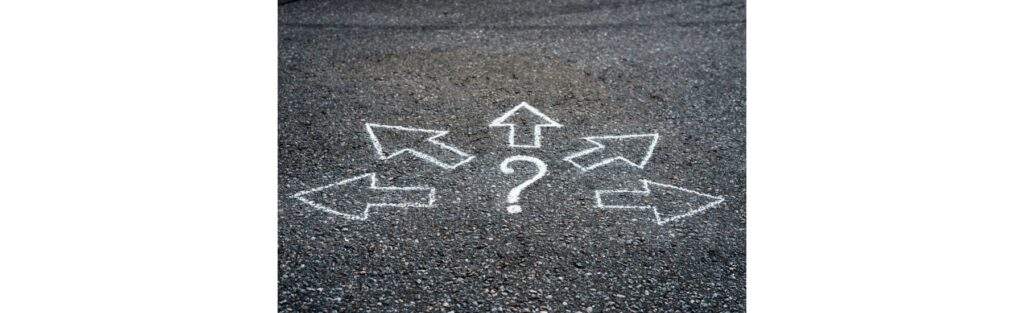 Gravel with painted white arrows pointing away in different directions from a centered question mark--Ubicación segura