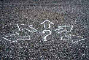 Gravel with painted white arrows pointing away in different directions from a centered question mark--Ubicación segura