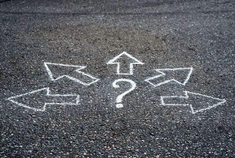 Gravel with painted white arrows pointing away in different directions from a centered question mark--Ubicación segura
