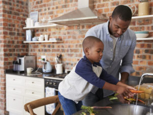 A father and son work together in a kitchen to clean vegetables in a sink
