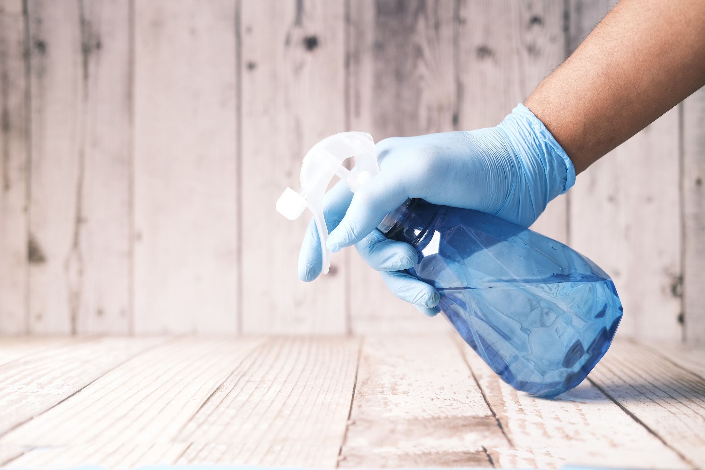 A gloved hand holds and uses a bottle of cleaning chemical spray.
