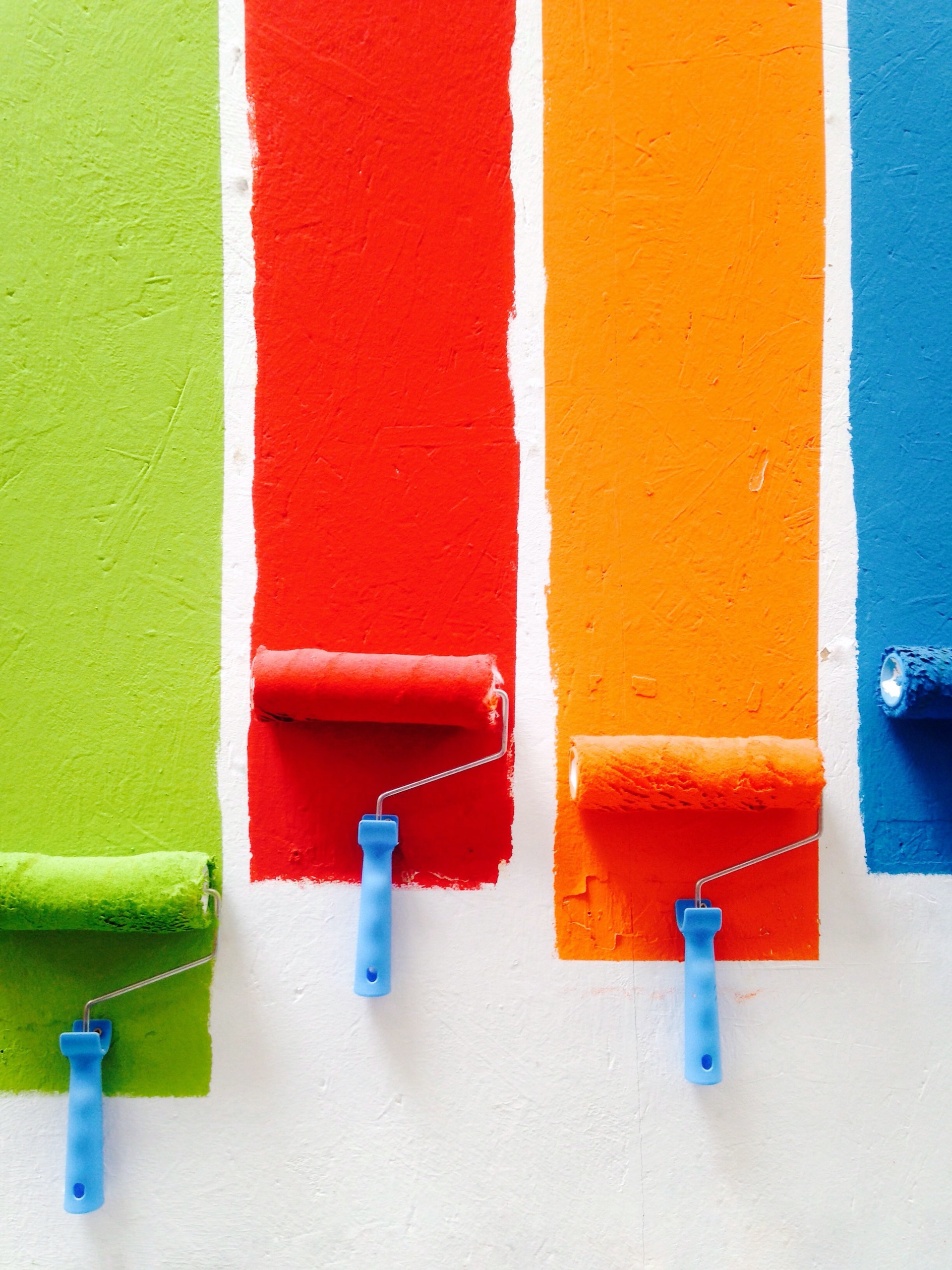 Different colored paint rollers on a wall.