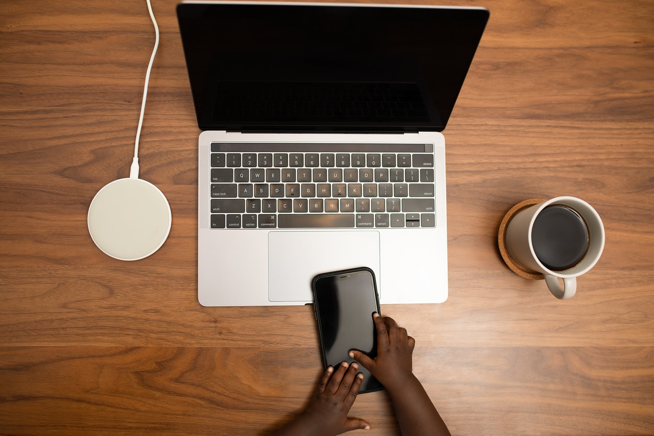 A baby's hand is touching a phone on a table, alongside and computer, phone charger and a mug--Radiation Exposure