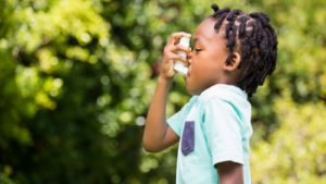 A young boy wearing a blue shirt uses an emergency inhaler