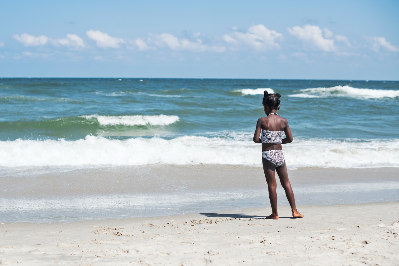 A young girl stands on the shore of a beach, looking out towards the ocean--sunscreen