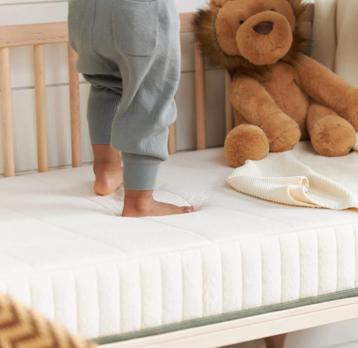 Child in PJs stands on crib mattress with a teddy bear in the background