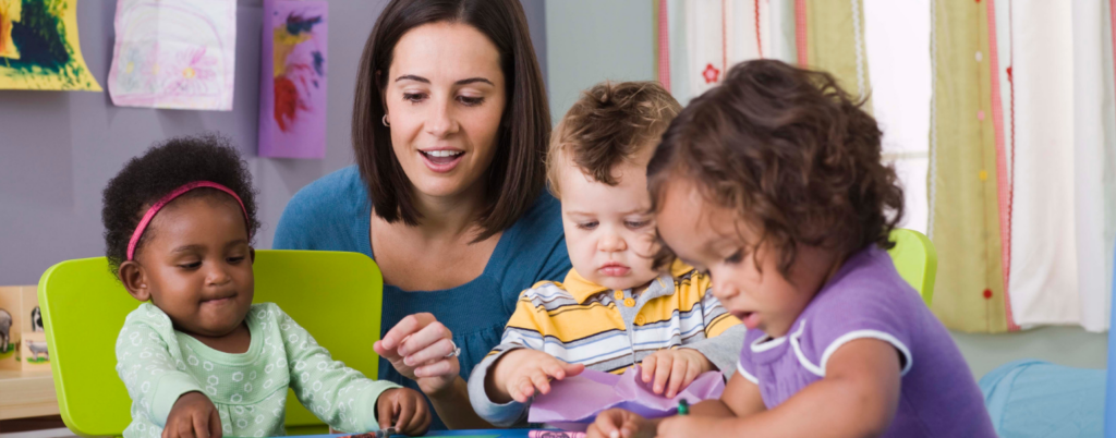 Woman interacting with three young children at a classroom table