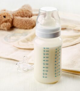 A picture of a baby milk bottle next to a pacifier, baby bib, and teddy bear--plastics