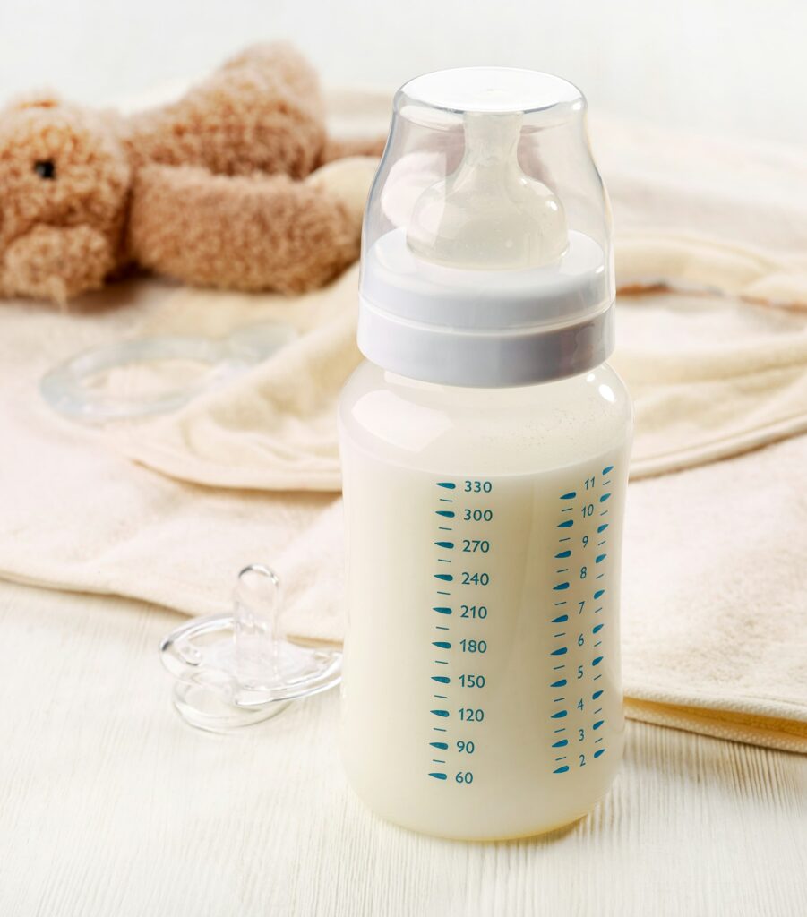 A picture of a baby milk bottle next to a pacifier, baby bib, and teddy bear--plastics