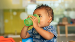 toddler drinks water out of a green plastic cup
