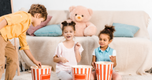 Three children eating popcorn out of red and white striped buckets in front of a couch----safer food packaging PFAS