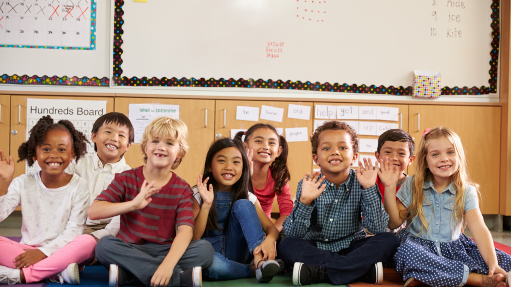 Children sitting in a group and waving at the camera - Iowa children's environmental health