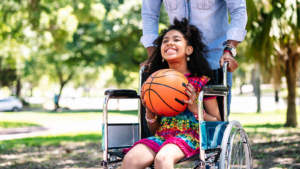 Child in wheelchair holding a basketball and smiling