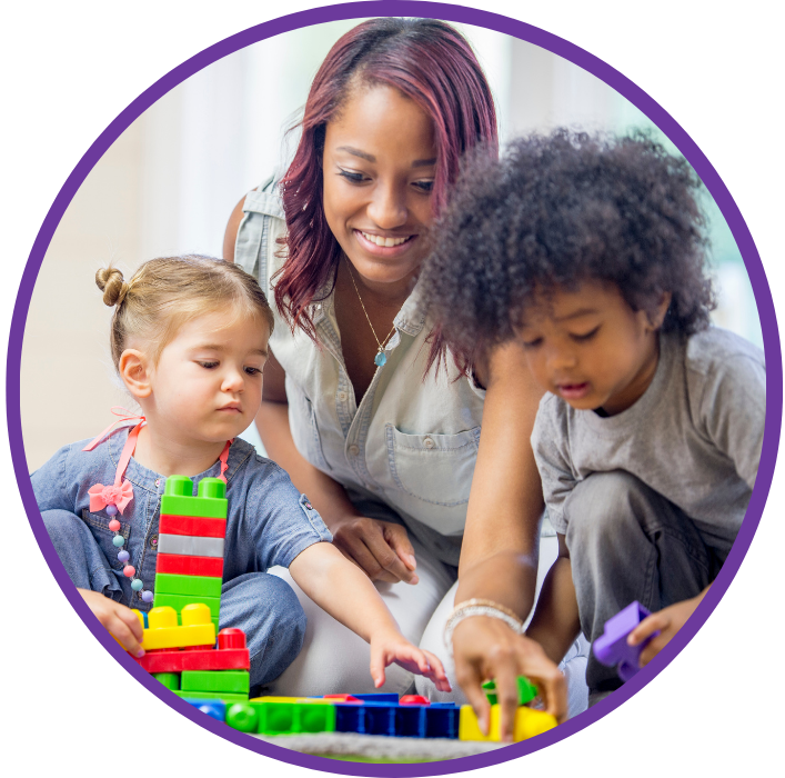 A woman sits on the ground with a young boy and a young girl, playing with plastic blocks